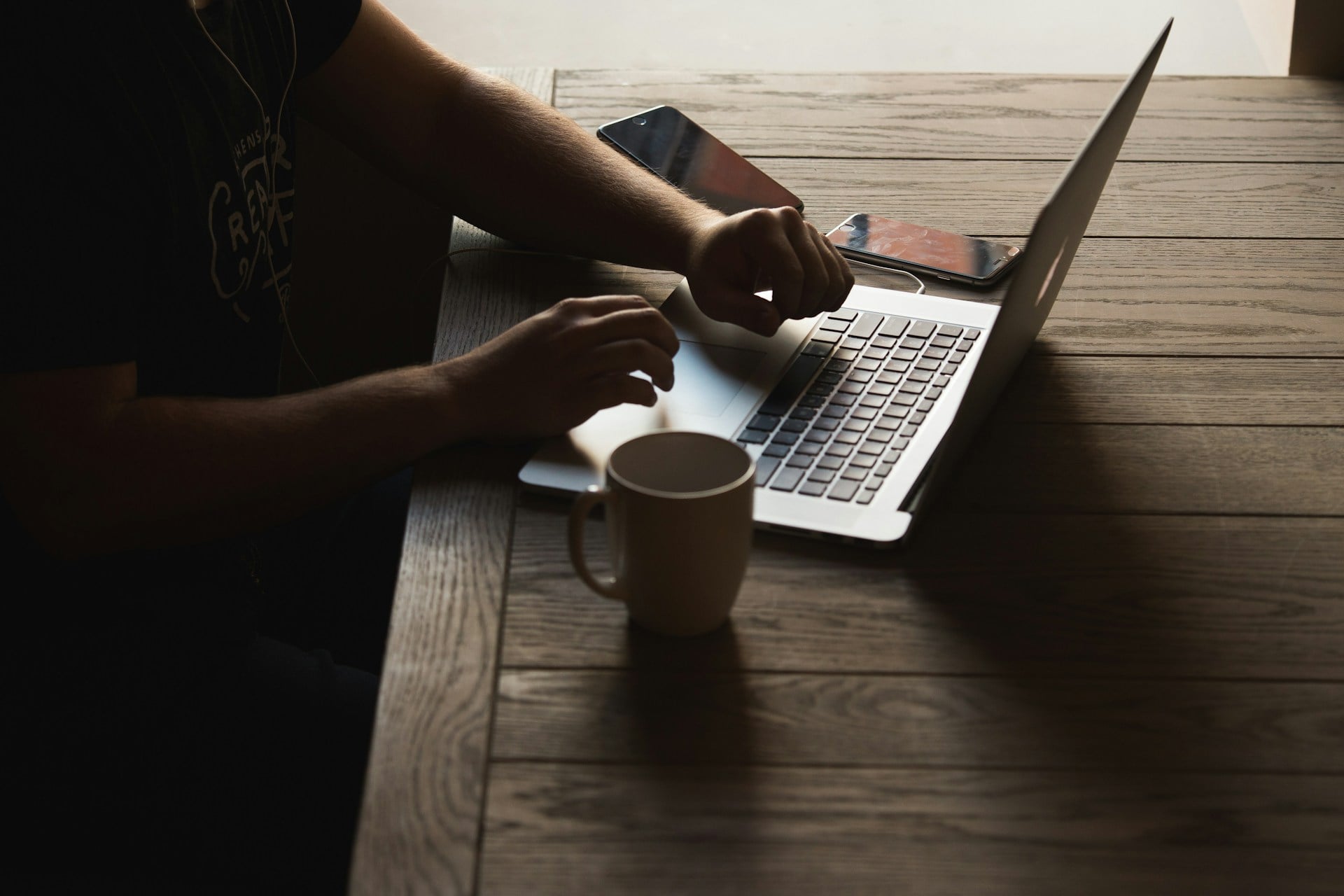 Hands typing on a laptop with a coffee mug on a wooden desk.